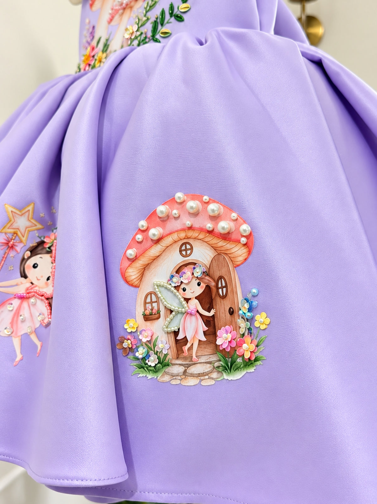 Close-up of the lavender birthday dress skirt featuring an enchanted mushroom house, fairy illustration, pearl embellishments and colourful flowers.