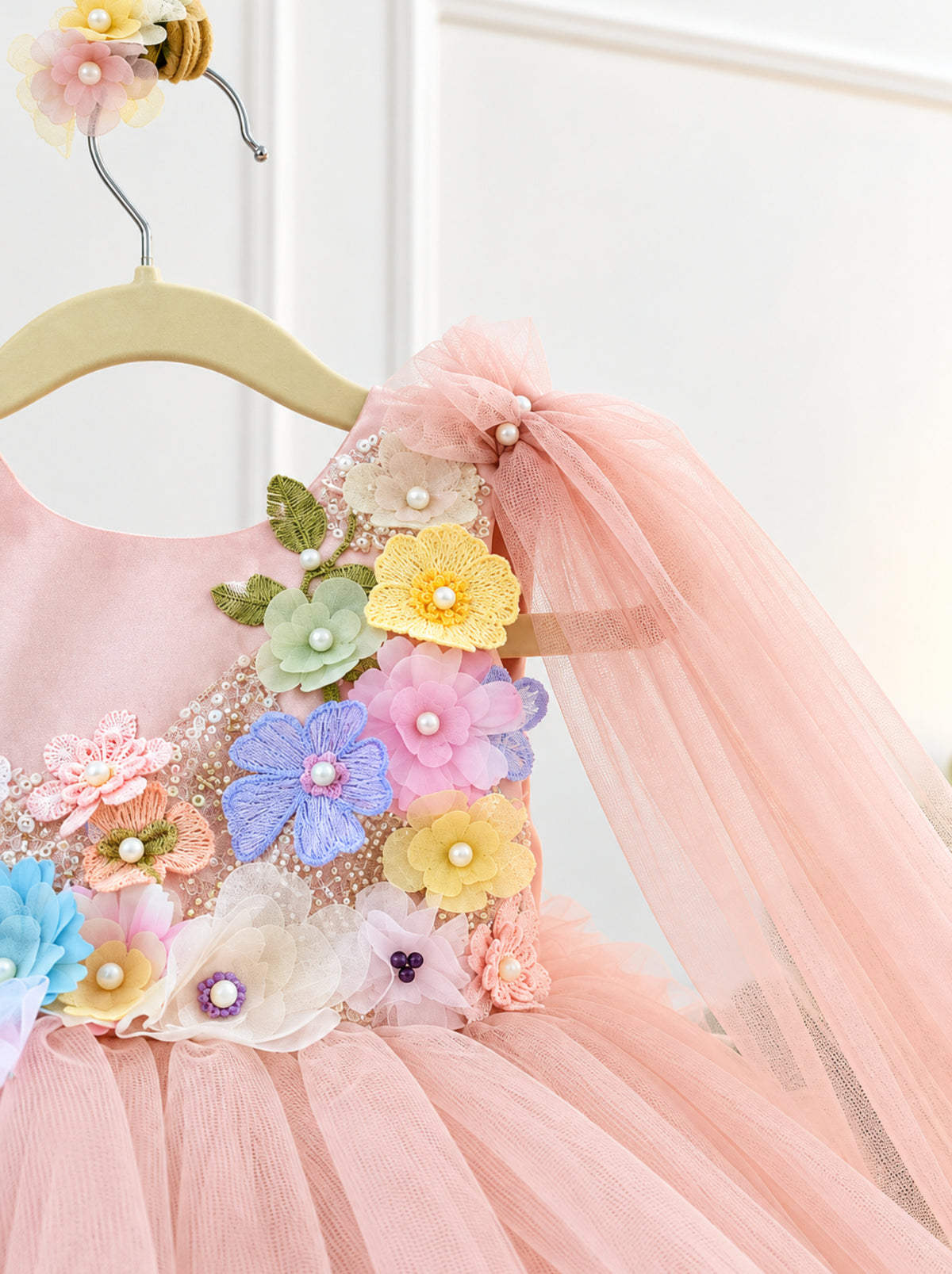 Pastel pink tulle shoulder drape with 3D floral appliqués and pearl details on girls dress