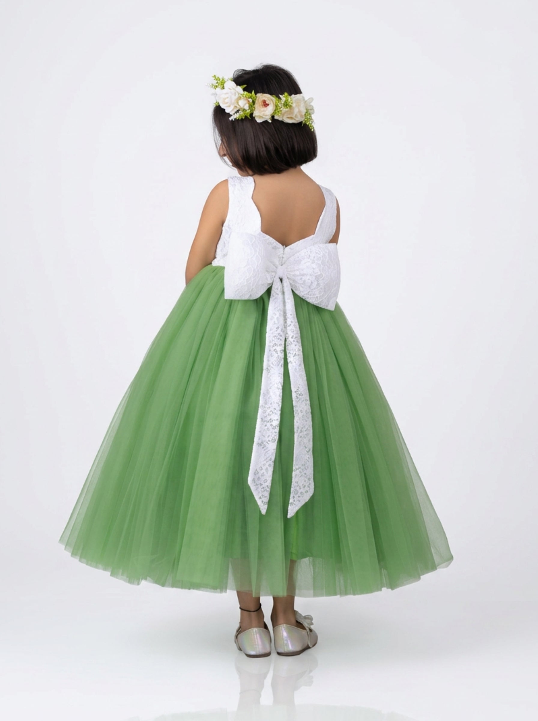 Elegant sleeveless flower girl dress with white bodice and voluminous green tulle skirt, styled with floral crown and roses.
